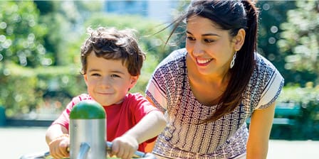 Petit garçon en train de jouer dans un parc sous le regard attentif de sa nounou