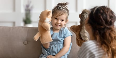 Petite fille jouant aux marionnettes sur un canapé avec sa nounou