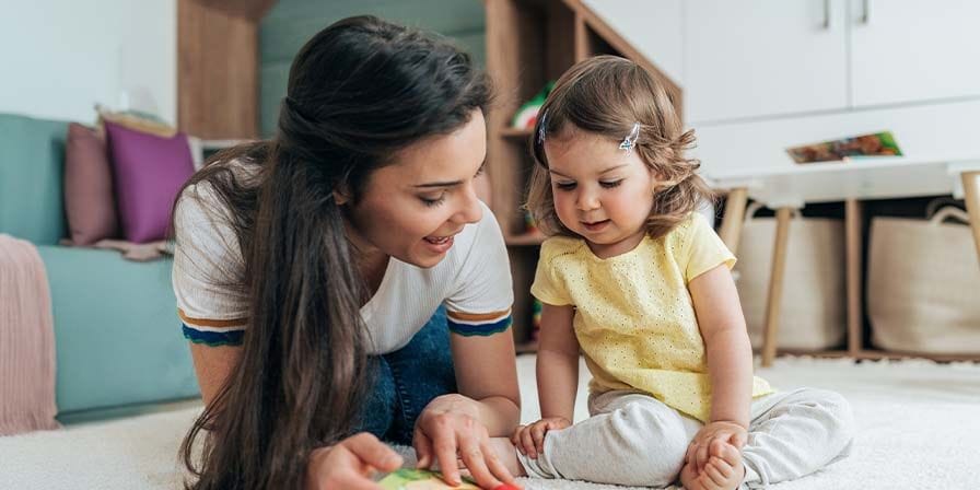 Nounou et enfant sur le sol, en train de regarder un livre