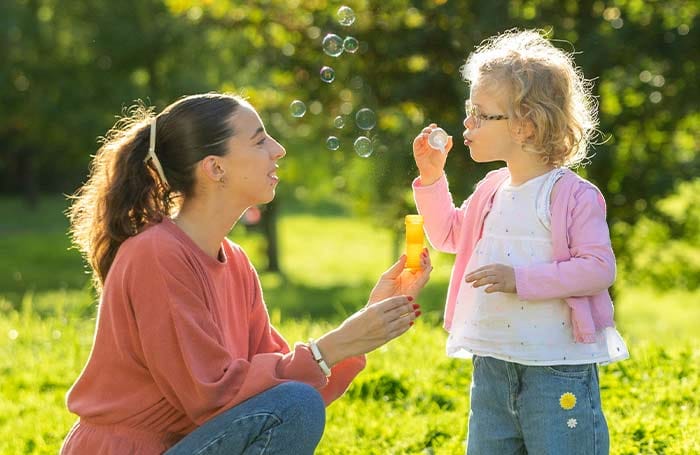 Nounou regardant une petite fille faire des bulles par un mercredi ensoleillé