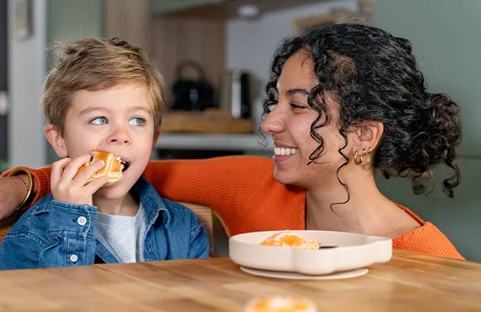 Nounou étudiante partageant un goûter avec un petit garçon mangeant une viennoiserie