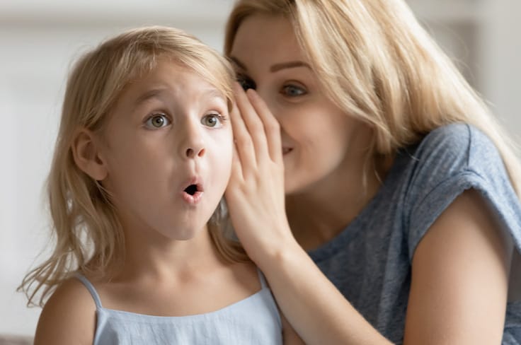 Nounou chuchote à l’oreille d’une petite fille, qui a l’air surprise